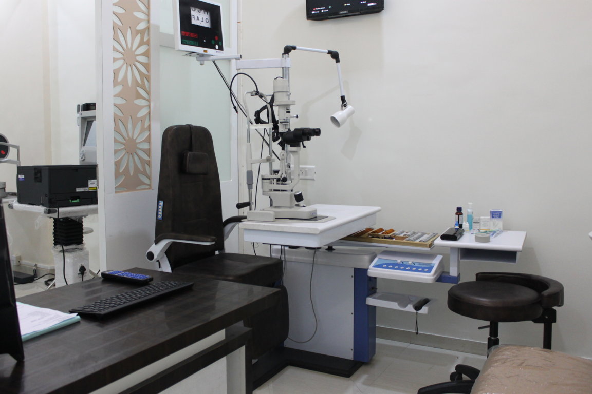 Slit-lamp examination room at Insight Institute with a Snellen acuity monitor mounted above the patient chair and a trial-lens shelf alongside